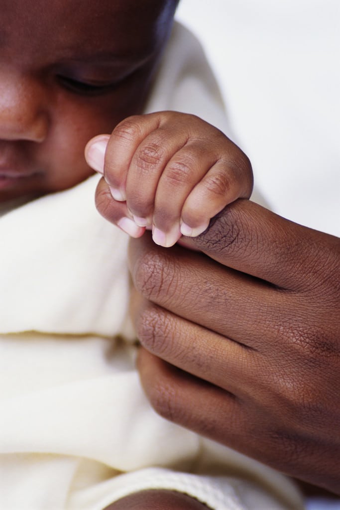 baby of african descent squeezing parent's finger