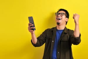 Man holding phone and punching air in excitement with huge smile on his face